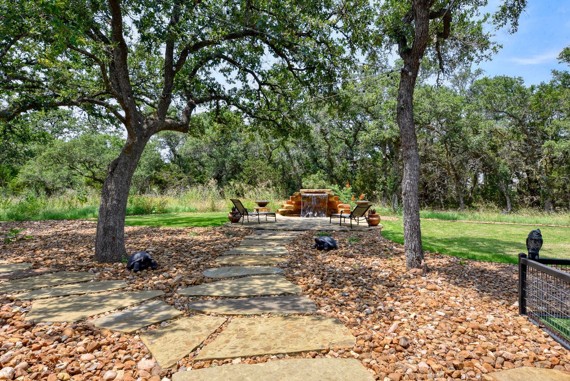 Garden path leading to patio with chairs and fountain.