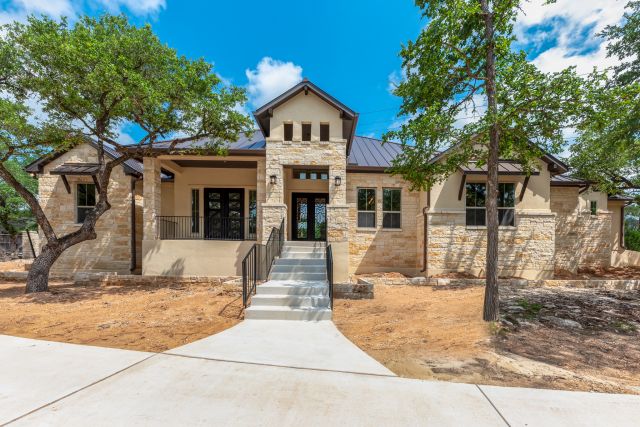 Modern stone house with trees and sunny sky.